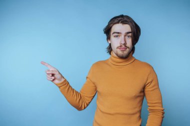 Hardal rengi süveter giyen genç adam mavi arka plana yan bakıyor..