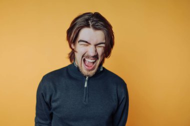 Uzun saçlı genç adam turuncu arka plana gülüyor..