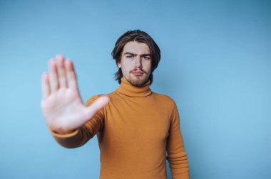 Turuncu süveterli bir adam mavi arka planda dur işareti yapıyor..