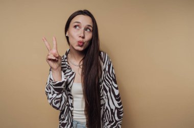 Bej arka planda neşeli bir ifadeyle barış işareti yapan bir kadın..