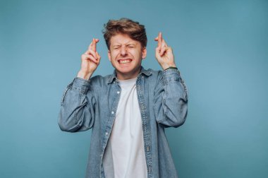 Parmakları çapraz genç adam, gözleri kapalı, şans umuduyla.