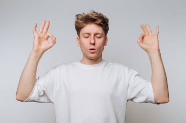 Genç adam gözleri kapalı meditasyon yapıyor, elleriyle tamam işareti yapıyor..
