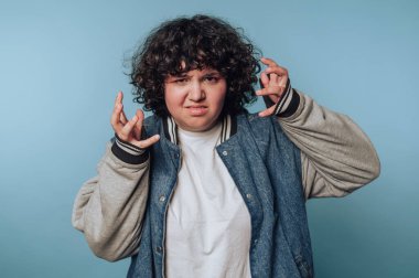 Kıvırcık saçlı biri mavi arka plana karşı sinirli bir ifade takınıyor..