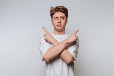 Beyaz tişörtlü kafası karışmış bir adam kollarını kavuşturup zıt yönlere bakıyor..