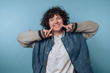 Mavi arka planda kot ceketli, kıvırcık saçlı, gülümseyen biri..