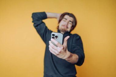 Adam sarı arka planda akıllı telefonuyla selfie çekiyor..