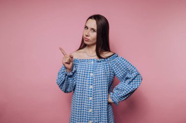Mavi kareli elbiseli kadın pembe arka planda parmak işareti yapıyor.