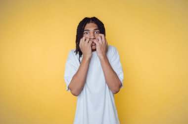 Saçları örülmüş biri sarı arka plana şaşırmış gibi görünür..