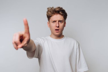 Beyaz tişörtlü genç adam şaşırmış bir ifadeyle işaret ediyor..