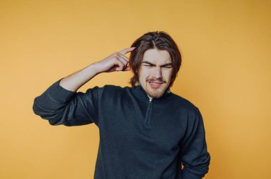 Siyah kazaklı bir adam sarı arka planda kafasını kaşıyordu..