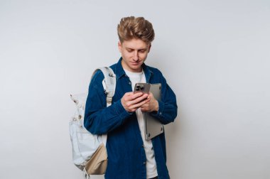 Sırt çantalı genç adam akıllı telefon kullanıyor, dizüstü bilgisayar tutuyor..