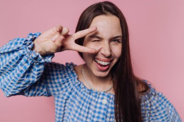 Mavi kareli bluzlu gülümseyen kadın barış işareti yapıyor.