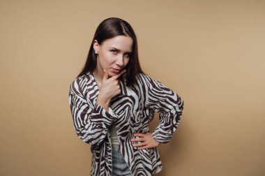 Zebra desenli gömlekli kadın bej arka planda düşünceli bir şekilde poz veriyor..
