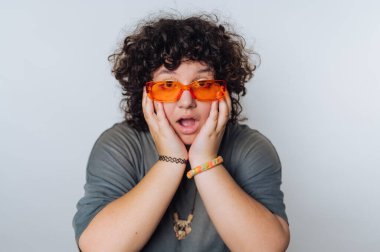 Kıvırcık saçlı, turuncu güneş gözlüklü, şaşırmış bir yüz ifadesi var.
