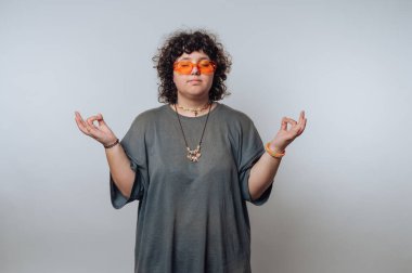 Turuncu güneş gözlüğü ve günlük kıyafetlerle meditasyon yapan biri..