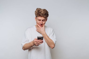 Beyaz tişörtlü genç adam akıllı telefona özenle bakıyor..