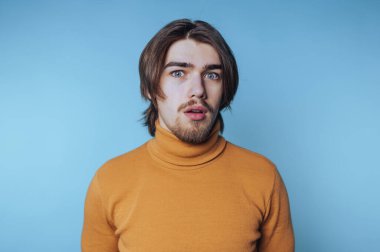 Turuncu balıkçı yaka giyen, şaşkın suratlı genç bir adam.