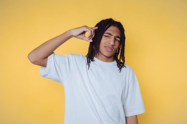 Sarı arka planda beyaz tişörtlü genç bir adam, kafası karışık ve düşünceli bir hareket yapıyor..