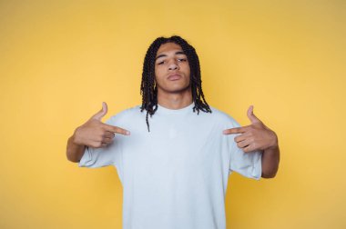 Sarı arka planda kendini gösteren örgülü saçları olan genç bir adam..