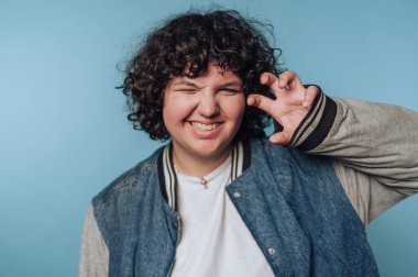 Mavi arkaplana karşı pençe hareketiyle şakacı poz veren kişi.