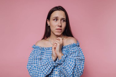 Mavi kareli elbiseli kadın pembe arka planda endişeli görünüyor..