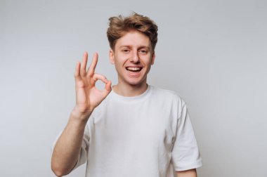 Beyaz tişörtlü genç adam elle iyi bir jest yapıyor..