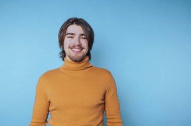 Hardallı balıkçı yakalı genç adam mavi bir arka plana gülümsüyor..