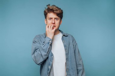 Tırnak yiyen genç bir adam, endişeli görünüyor, kot ceket giyiyor..