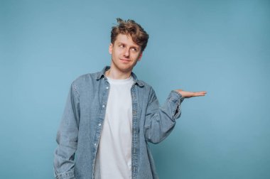 Kot gömlekli bir adam mavi arka planda el kol hareketi yapıyor..