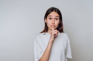 Beyaz tişörtlü genç bir kadın susma hareketi yapıyor..