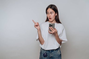 Akıllı telefon tutan, yan bakan, şaşırmış yüz ifadesi olan genç bir kadın..