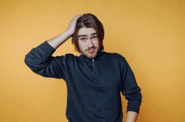 Turuncu arka planda uzun saçlı, düşünceli bir genç adam..