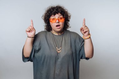 Kıvırcık saçlı ve yukarı bakan turuncu güneş gözlüklü biri..