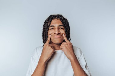 Saçları örgülü, gülümseyen ve yanaklarını bastıran bir genç..