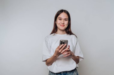 Gündelik kıyafetli genç bir kadın elinde akıllı bir telefonla, gülümsüyor..