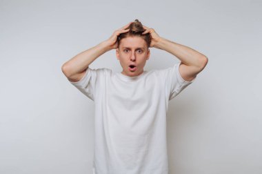 Beyaz tişörtlü, elleri kafasında şaşırmış genç bir adam..