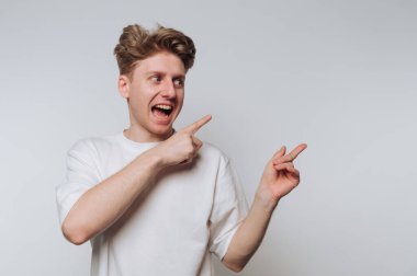 Beyaz tişörtlü genç adam gri arka plana bakıp gülümsüyor..