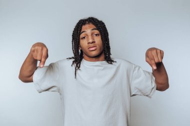 Saçları aşağıya doğru örülmüş genç bir adam. Tarafsız bir arkaplanda düz beyaz bir tişört giyiyor..