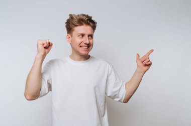 Beyaz tişörtlü genç adam beyaz arka plana bakıp gülümsüyor..