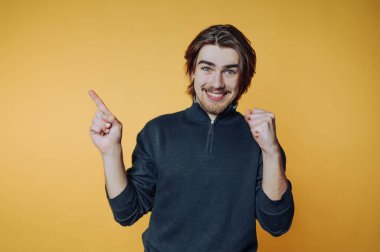 Sıradan süveter giyen gülümseyen adam sarı arka planda işaret ediyor ve işaret ediyor..