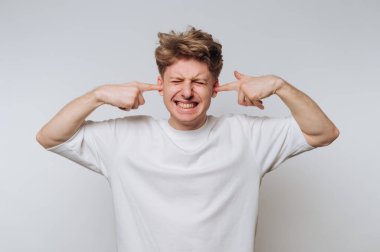 Beyaz gömlekli genç adam kulaklarını parmaklarıyla kapatıyor, gözleri kapalı..