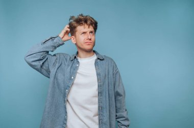 Sıradan kot gömlekli bir adam kafasını mavi arka plana sürtüyor..