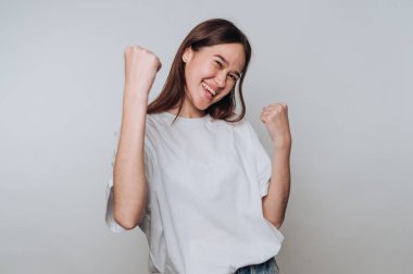 Beyaz tişörtlü neşeli bir kadın yumruklarını sıkarak kutluyor..