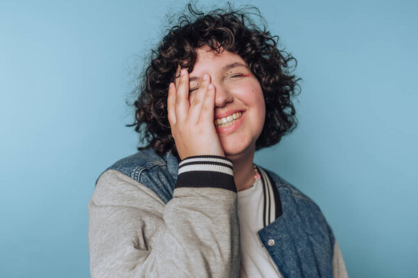Smiling person with curly hair covering face, wearing a jacket.