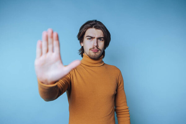 Man in orange sweater making a stop gesture against blue background.