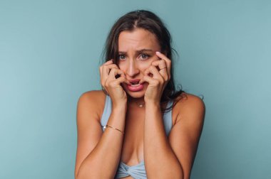 Mavi arka planda elleri yüzü olan endişeli bir kadın..