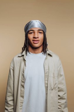 Bej arka planda durag ve günlük gömlek giyen genç bir adam..