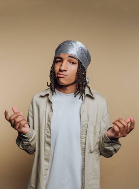 Saçları örgülü ve bandanalı genç bir adam, tarafsız bir arkaplanda günlük kıyafetler giyiyor..