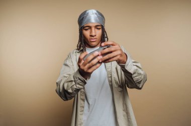 Saç örgülü genç bir adam durag takıyor, akıllı bir telefona odaklanmış..