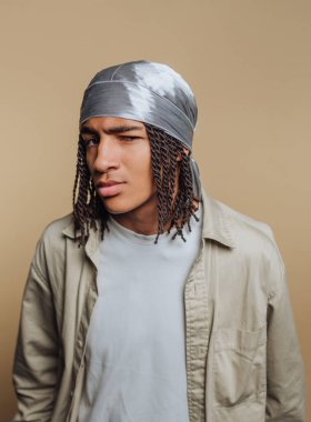 Saçları örgülü, bandana takan, kuşkucu görünen genç bir adam..